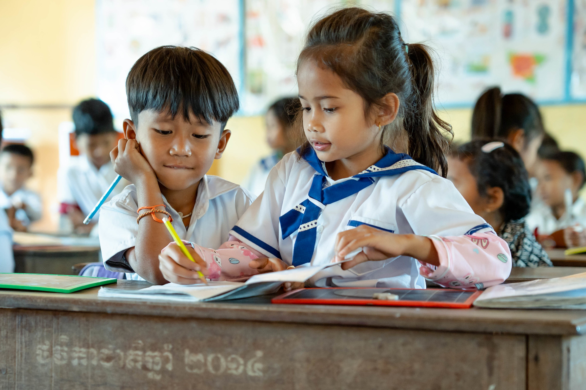 Two Cambodian Students working together in a workbook, wearing white and blue school uniforms