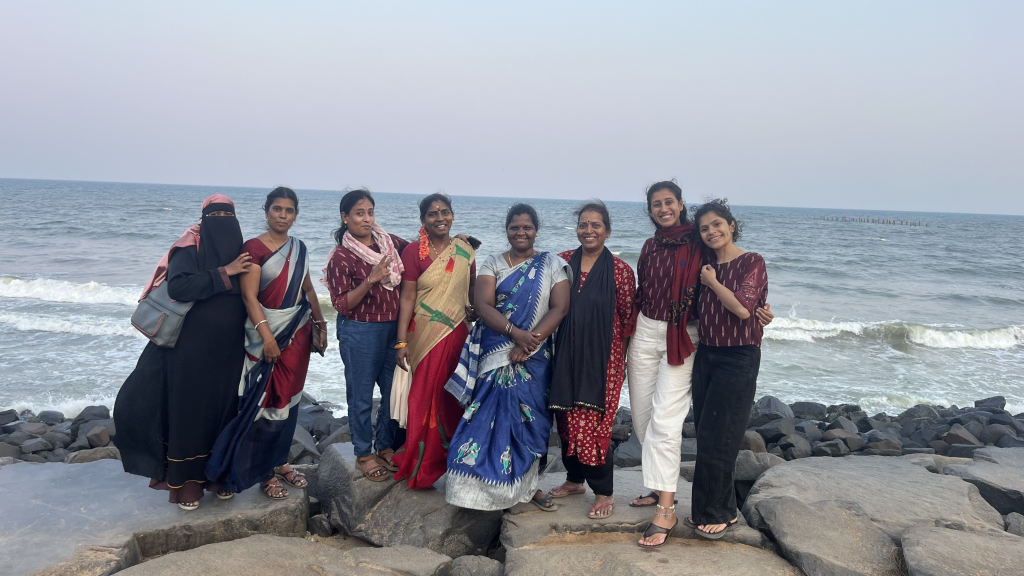 Group of women wearing colourful sarees standing in front of large body of water